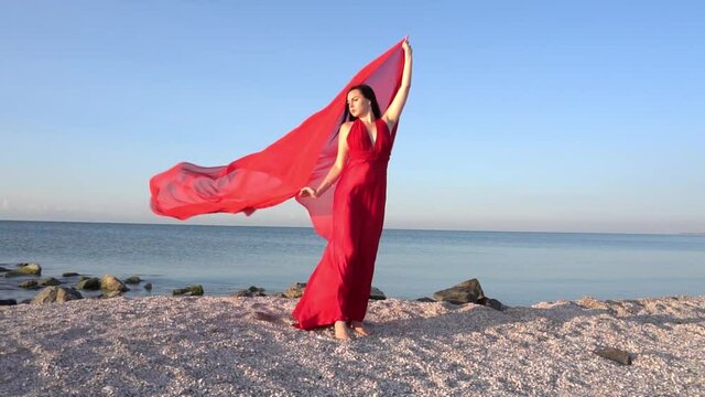 Slow Motion Woman in a red dress in the wind along beach by the sea or ocean