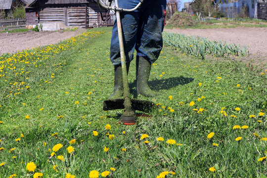 Green lawn on a spring day against the background of a working lawn mower and feet in boots, side view-the concept of carrying out spring seasonal work in the garden