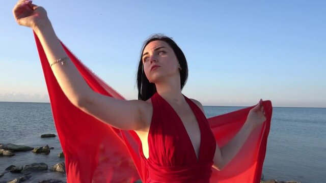 Beautiful woman posing in a luxurious red dress with a long train standing at th