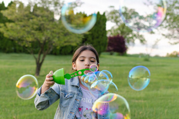 Hispanic girl playing in the park blowing soap bubbles