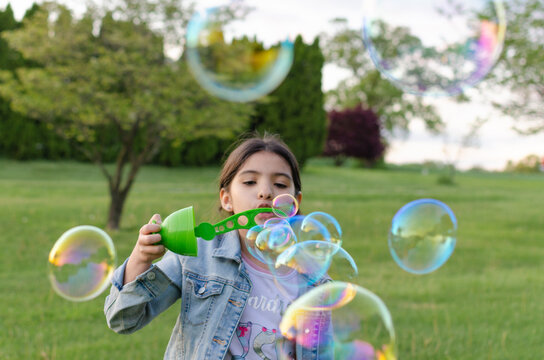 Hispanic Girl Playing In The Park Blowing Soap Bubbles