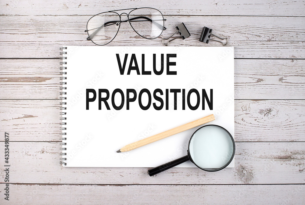 Poster notebook with text value proposition on the wooden table with pen, magnifier and glasses