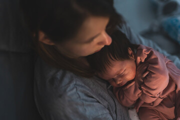 Close up portrait of newborn cute caucasian baby girl or boy in hands of mother putting to sleep at night in dark room - affection bonding motherhood parenthood and care concept © Miljan Živković