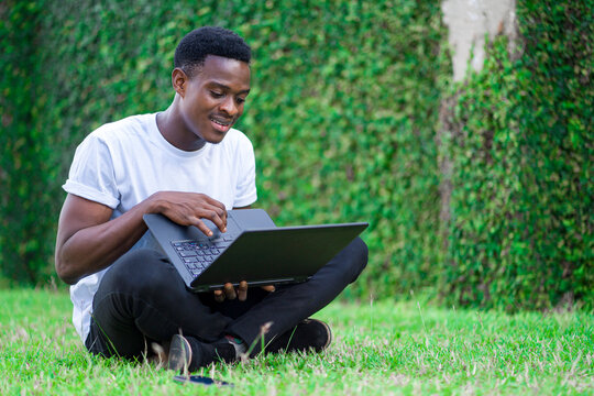 image of cheerful african guy with laptop, sitting in a lawn with crossed legs