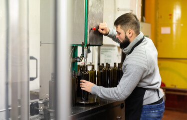 Naklejka na ściany i meble Young entrepreneur engaged in olive oil production, controlling process of bottling of finished product in glass bottles