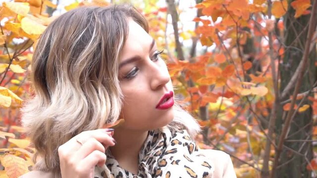 Luxury blonde girl with beautiful hair in a coat holding a maple leaf in autumn