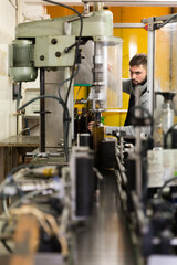Young bearded man working on bottling line of artisanal olive producing oil factory