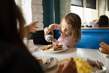 Mother with toddler daughter pouring ketchup in diner