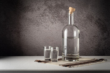 A glass bottle with glasses, a strong drink, on a white countertop against a gray wall