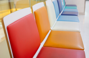 Selective focus shot with copy space of many colorful chairs in a row in the lobby or waiting room in hospital shows joyful, comfortable, clean, bright and happy atmosphere for seated people.