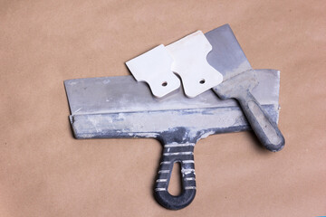 Construction metal spatulas in mortar after work. Dirty tool on craft brown paper. For laying tiles, cement, grouting and more. Indispensable for home renovation. Metal and plastic