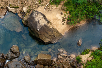 Closeup of the base of the Pinaisara waterfall seen from the top with beautiful natural pool, lush vegetation, rock formations, trail signage on the ground. Iriomote Island.