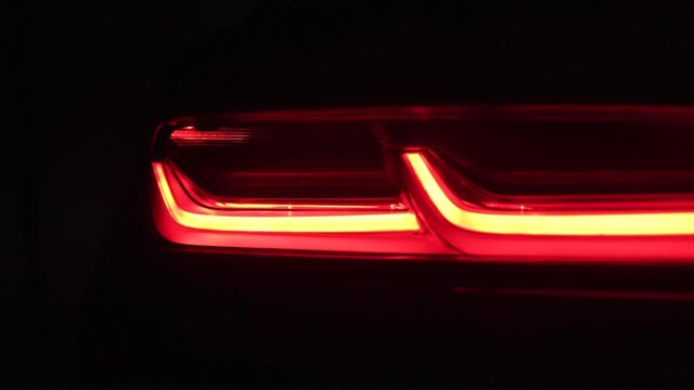 Car taillight in the dark night. Rear view of modern, red, glowing, luxury, auto LED tail lights in garage.