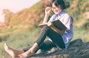cute asian little girl with glasses reading a book in garden at summer time