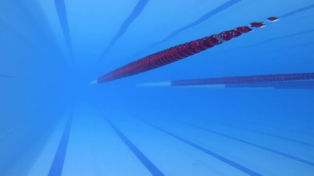 Lots of clear bubbles in the clean water pool. A girl in a black swimsuit dives into the water from a height. Indoor pool, standing water. High quality. 4k footage.