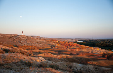 the lighthouse on the sandstone hill during sunset with the moon