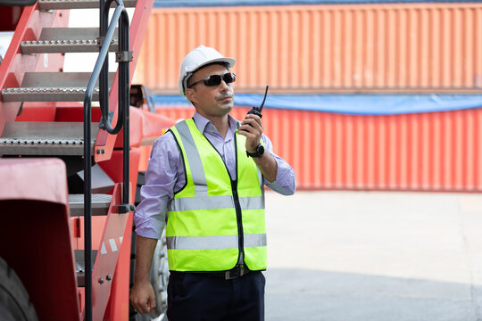 factory worker or engineer using walkie talkie for preparing a job beside truck in containers warehouse storage