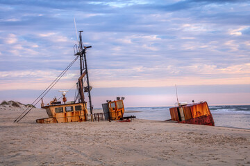 Rustic shipwreck being swallowed up by the sand with sunrise clouds