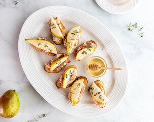 Top down view of a platter of crostini bites topped with sliced pear and prosciutto and thyme.