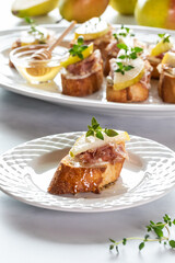 Close up view of a pear and prosciutto crostini appetizer with a platter of the same in behind. 