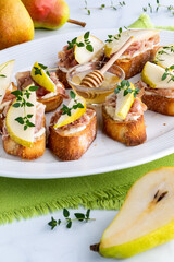 A platter of pear and prosciutto appetizers topped with thyme, and a half pear in front.