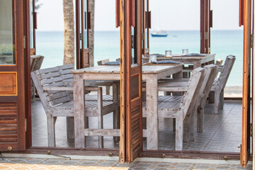 Wooden table and chairs in empty beach cafe next to sea. Thailand