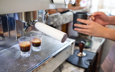 Closeup image of barista steaming milk while making latte coffee from coffee machine in cafe