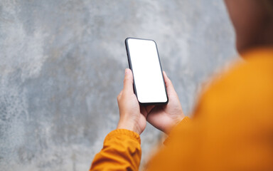 Mockup image of a woman holding mobile phone with blank white desktop screen in the outdoors