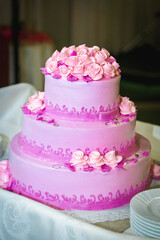 Large three-tiered pink cake decorated with cream flowers. On the table. Close-up.