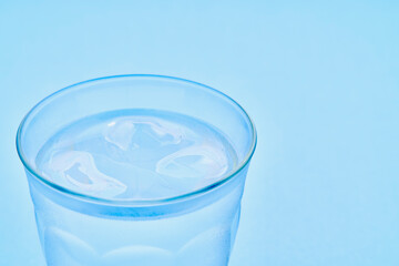 水色をバックに水滴のついた氷の入った冷たいグラス