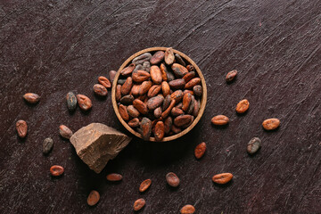 Bowl with cocoa beans on color background