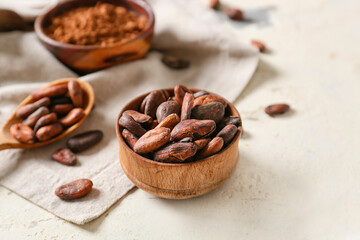 Bowl with cocoa beans on light background