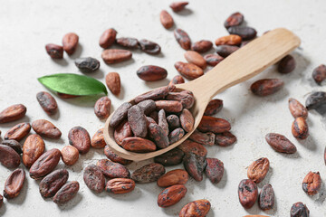 Wooden spoon with cocoa beans on light background