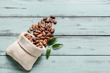 Bag with cocoa beans on color wooden background