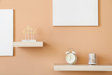 Fototapeta na wymiar Shelves with alarm clock and decor hanging on color wall