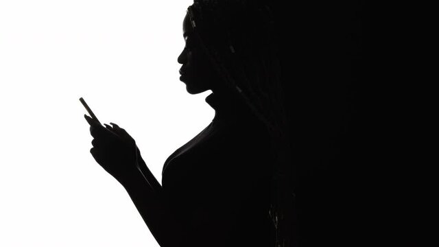 Social network. Silhouette black woman. Mobile input. Internet opportunities. Chatting communication. Concentrated profile african lady scrolling smartphone isolated white copy space.