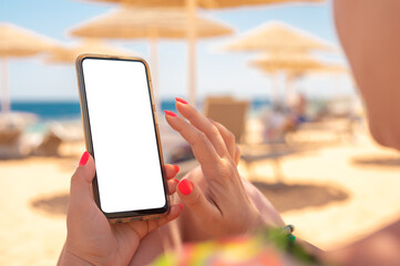 mockup image. woman use cell phone on beach, summer holiday. woman holding mobile phone with blank desktop screen on the beach. Mobile phone in female hand on the background of the resort beach