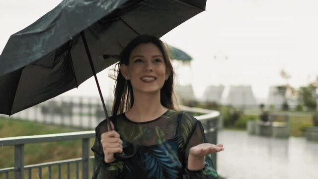 Pretty lady with umbrella holds hand under rain drops