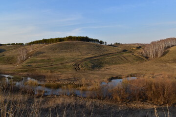 Fototapeta premium Beautiful landscape in early spring. View of hilly terrain, trees, country road and stream.