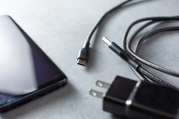 A closeup view of a power cord and plug next to a cell phone.