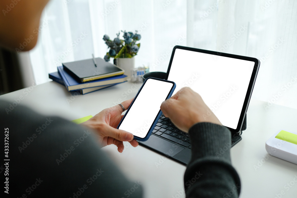 Poster close up over shoulder view of businessman sitting in front of computer tablet and using mobile phon