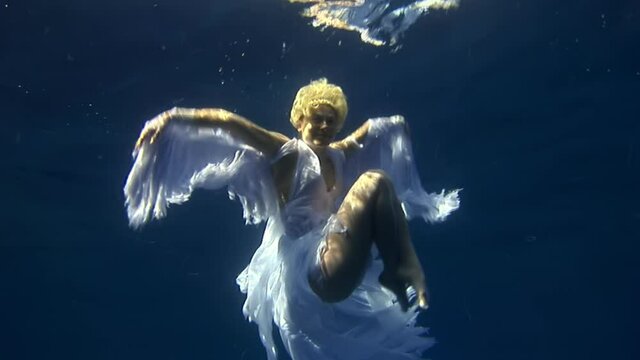 Young woman underwater model in white cloth on background of blue water. Concept of creativity and art of creating images.