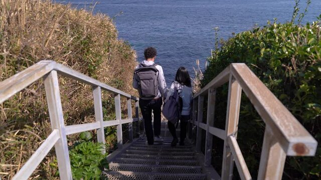 Couple walking down wooden stairs towards ocean. Back view