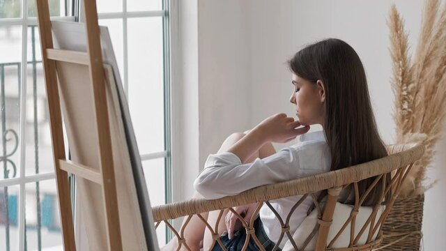 Upset young woman looks out of window sitting in art studio