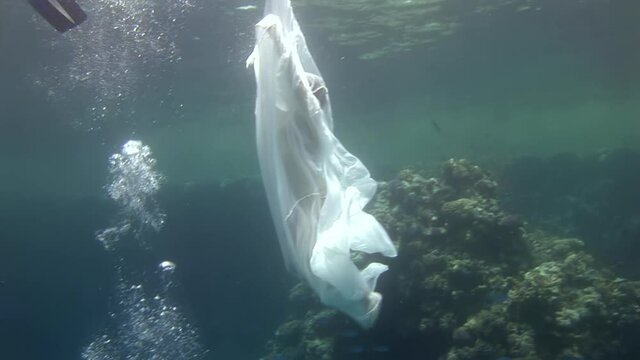 Birth of an angel in creation of underwater model freediver. Creativity and art of creating images on background of seabed. Young woman in white cloth.