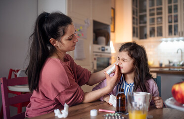 Obraz na płótnie Canvas Mother looking after sick small daughter at home, using nasal spray.