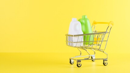 Shopping cart with bottles inside on a yellow background, closeup. Black Friday Shopping and Discount Concept