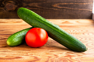 two cucumbers and one tomato on a wooden background