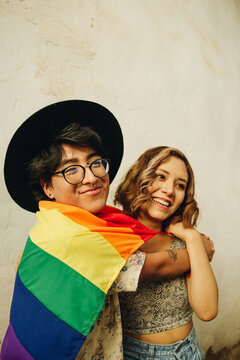 Amigos queer y bisexual abrazados y sonriendo  con la bandera LGTQB en la calle 