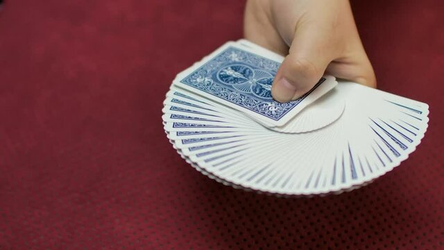 Slow motion close up of a magician spreading a deck of cards on a red background.